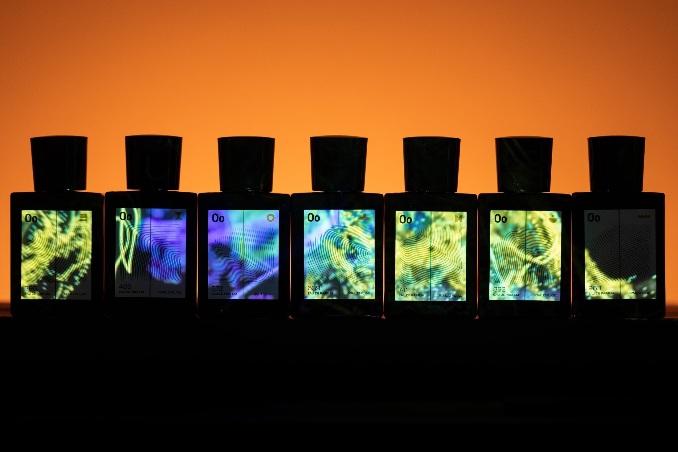 Seven Oo La Lab Fragrance & Frequency bottles displayed in a row, their labels lit in colour.